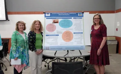 Three UNE faculty members stand next to a research poster